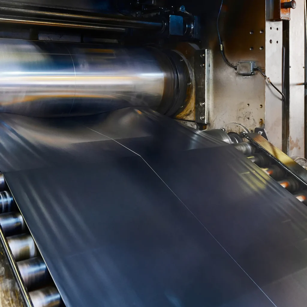 A wide belt of raw rubber compound moves along a roller conveyor